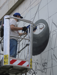 907087 Afbeelding 'street artist' 'Erwtje' op een hoogwerker bezig met het maken van een graffitikunstwerk op de wand ...